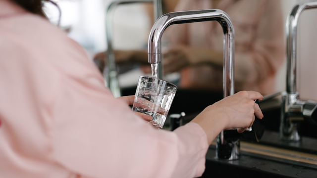 A person taking water from a kitchen sink.