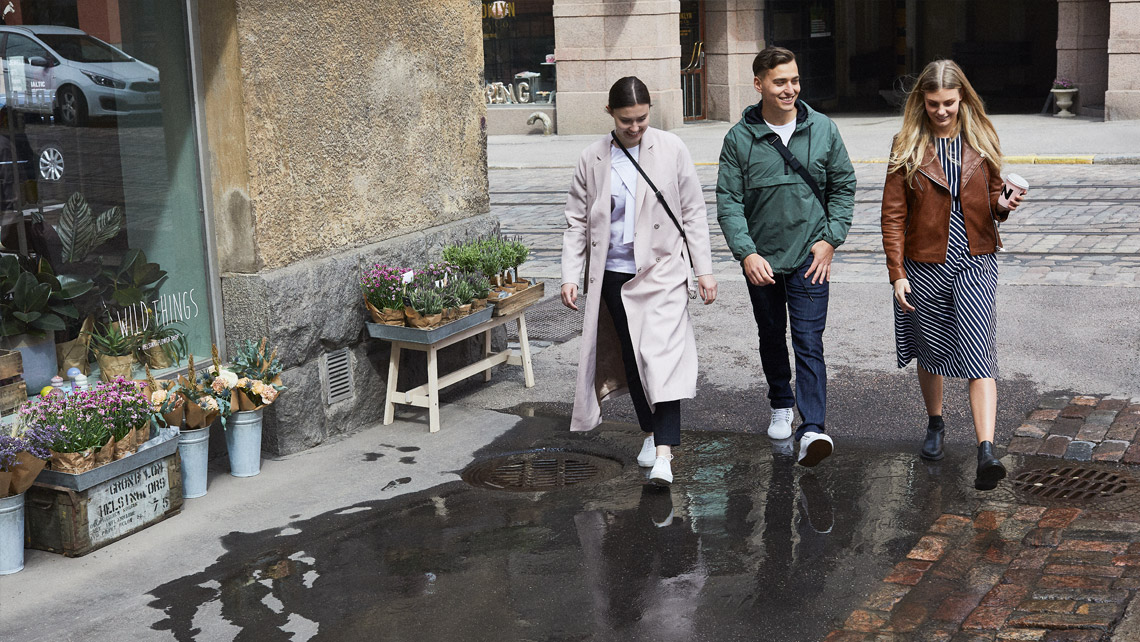 Three persons walking in a street on a wet asphalt.