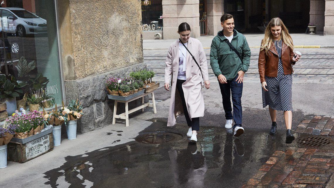 Three persons walking in a street on a wet asphalt.