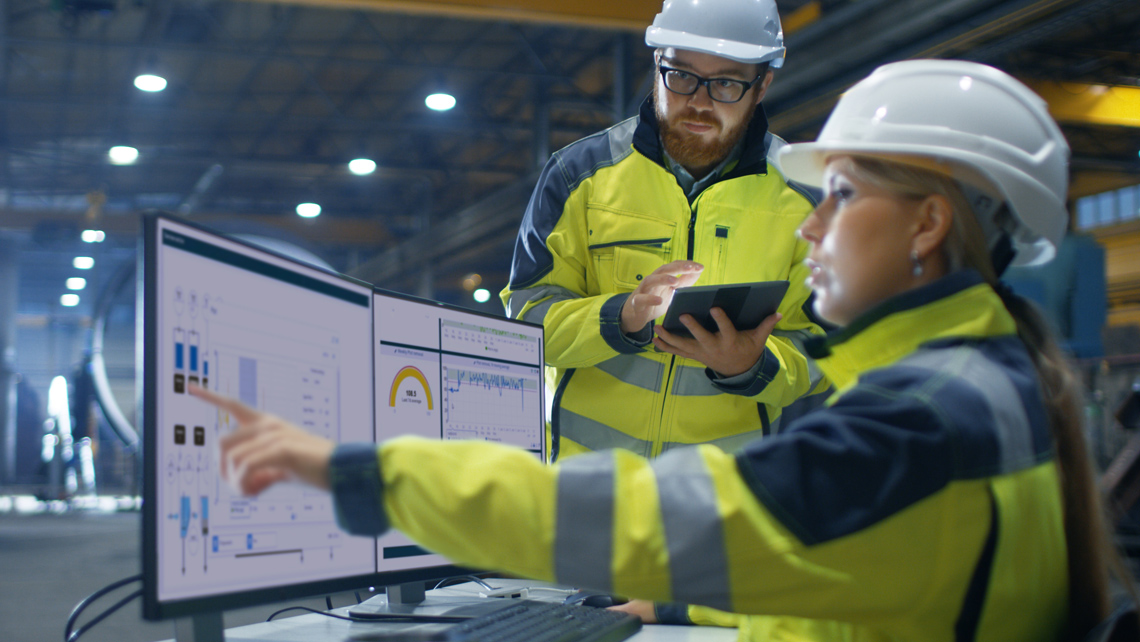 Two factory workers focusing on a monitor and dashboard.