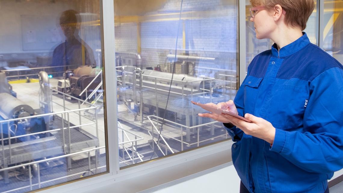 A factory worker holding a tablet and observing the production.