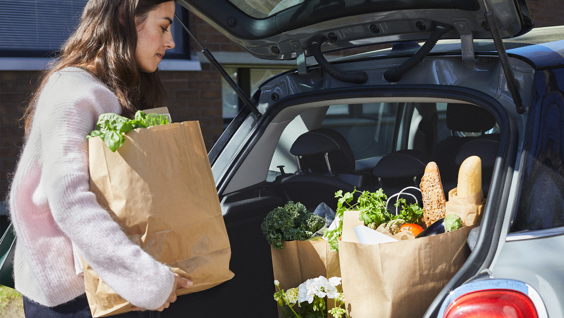 A person putting grocery shopping to a car trunk.