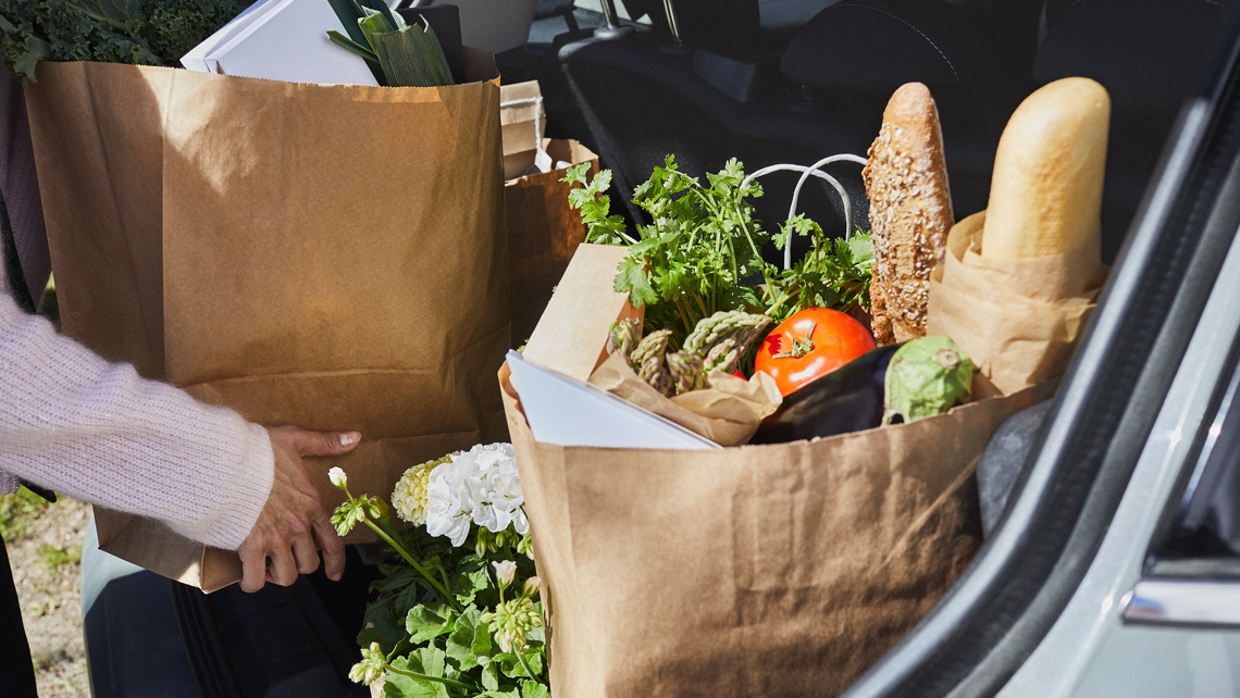 A person putting grocery shopping to a car trunk.