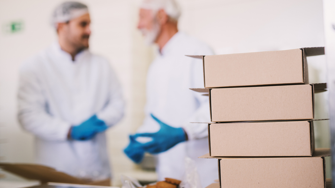 Pile of brown packages and two factory workers behind.