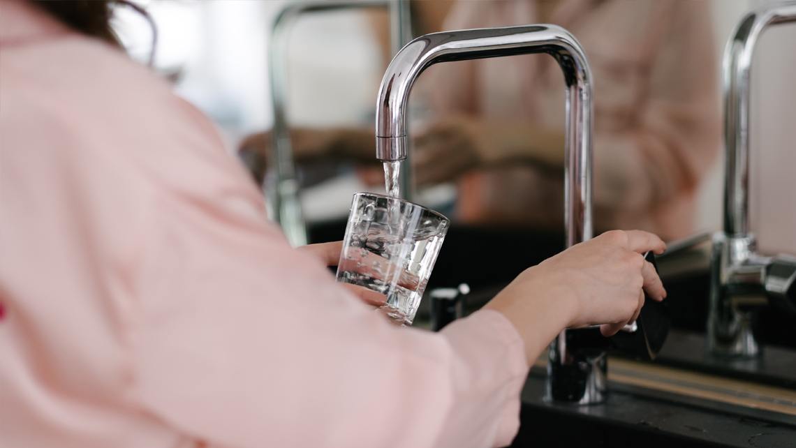 A person taking drinking water from a kitchen tap.
