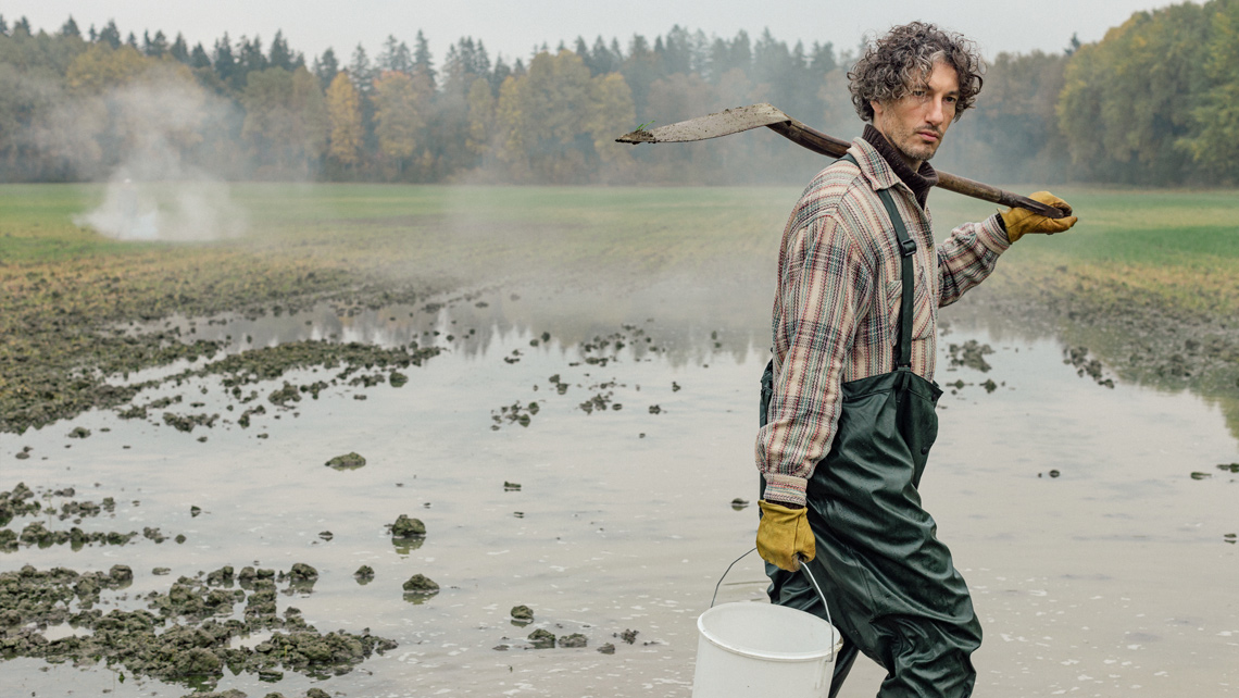 A farmer walking on the wet field.