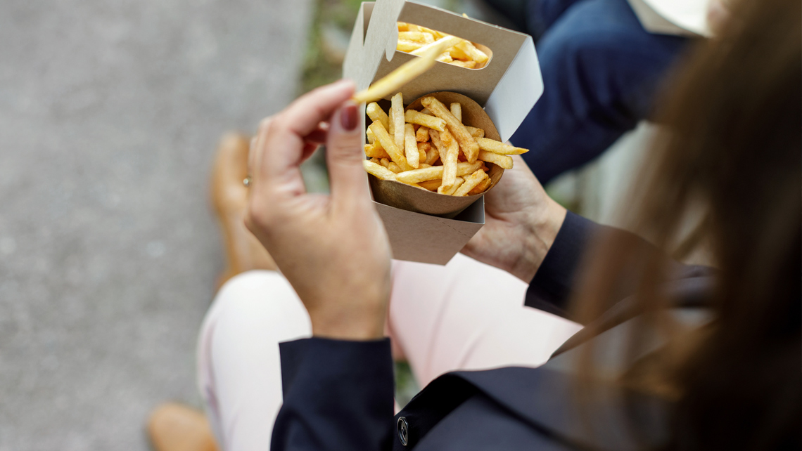 A person eating fries from a brown cardboard box.
