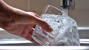 A person holding a glass under pouring tap water.