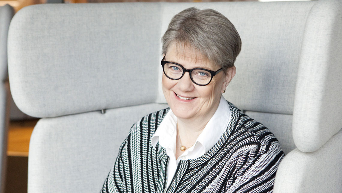 Woman with sort grey hair black glasses and smiling at the camera.