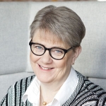 Woman with short grey hair and black glasses smiling at the camera.