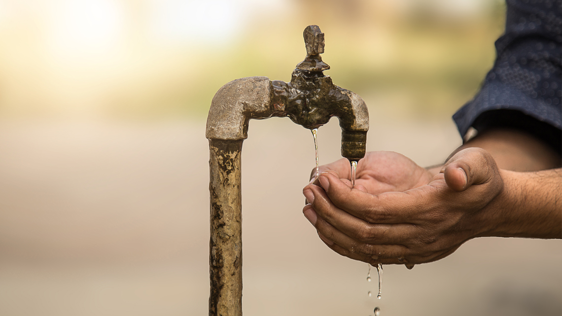 Cupped hands under water from old rusty tap.