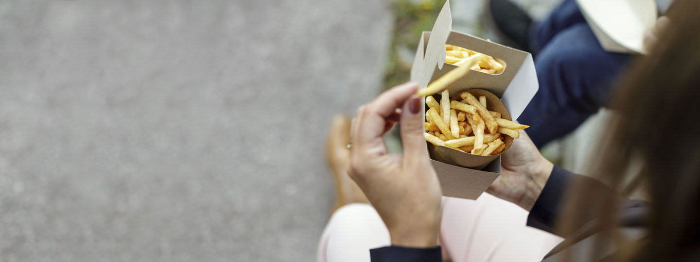A person eating french fries from a board package.