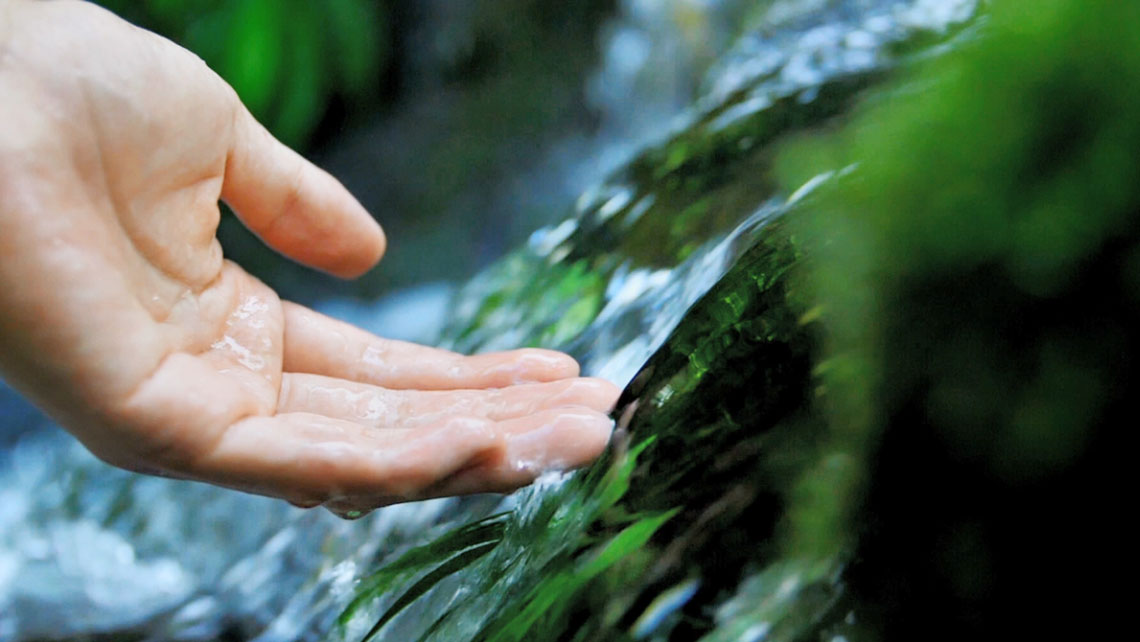 Hand reaching for water in waterfall