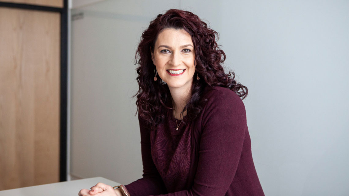 Woman with long dark curly hair and purple dress smiling at the camera.