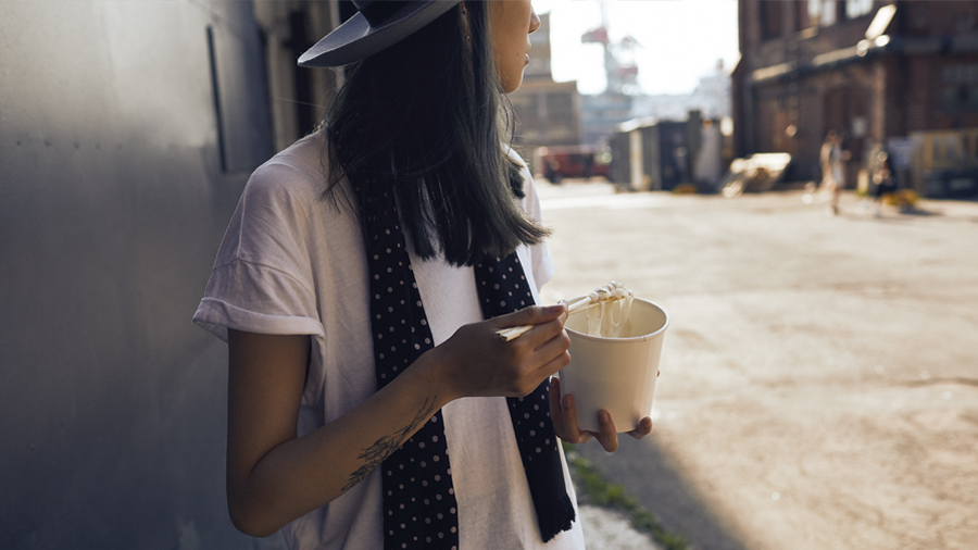 A person holding takeaway noodles in a paper cup.