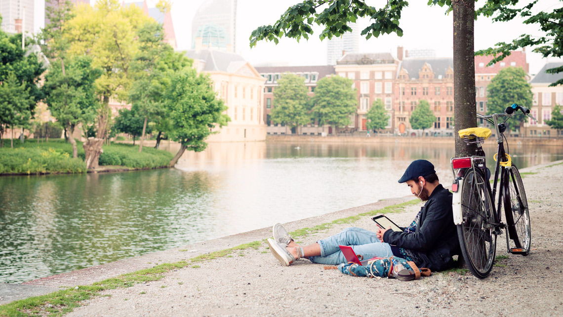 A person sitting by the river and reading a tablet computer.