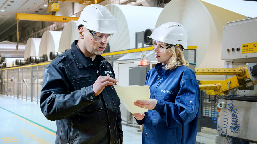 Two workers looking at a paper in front of paper machine.