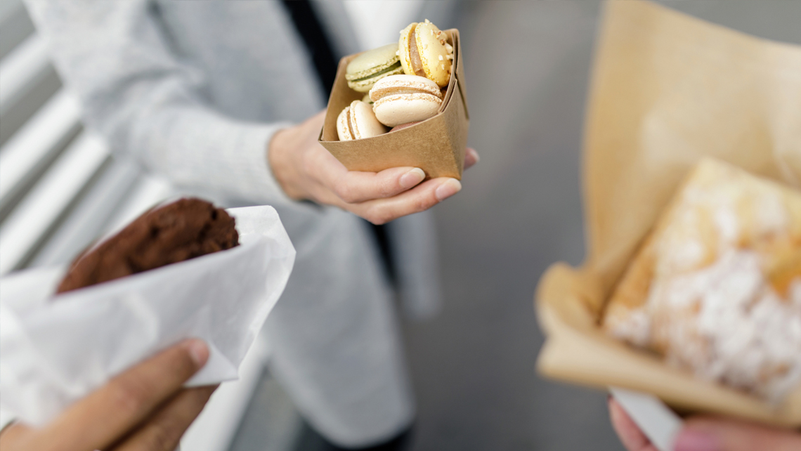 Three persons holding sweets in a brown paper.