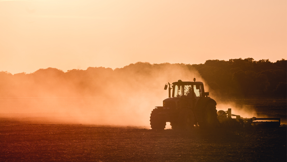 Tractor cultivating dry field in a burning evening sunshine.