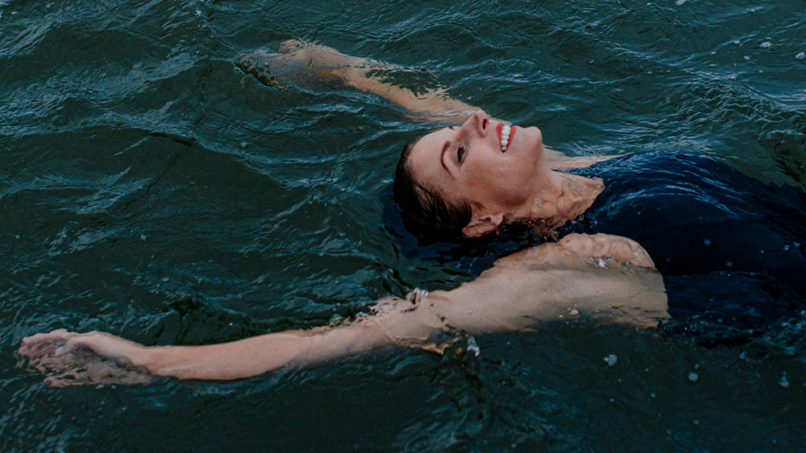 Woman in bathingsuit smiling while floating in the sea with arms wide spread.