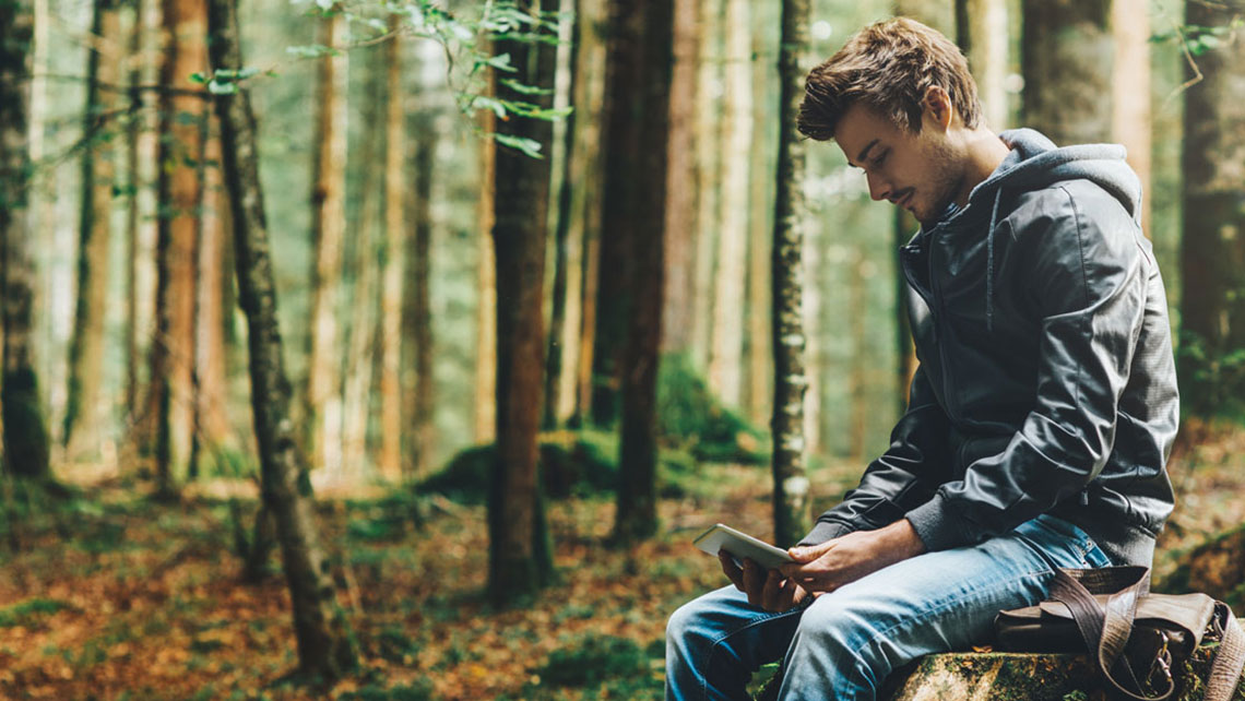 Person sitting in the forest and holding a tablet computer.