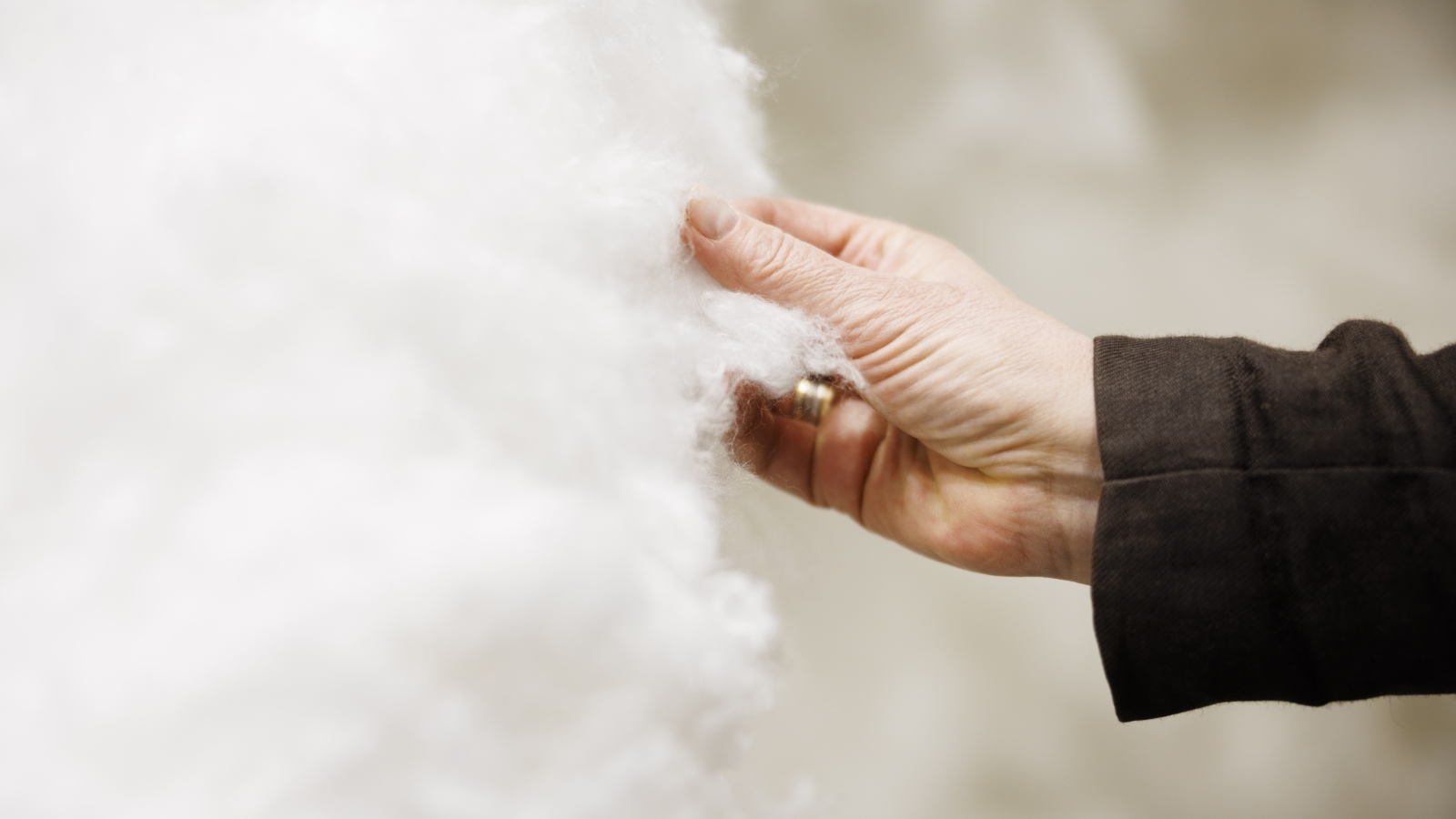 Close-up of a hand touching soft, fluffy white material, highlighting texture and detail against a blurred background.