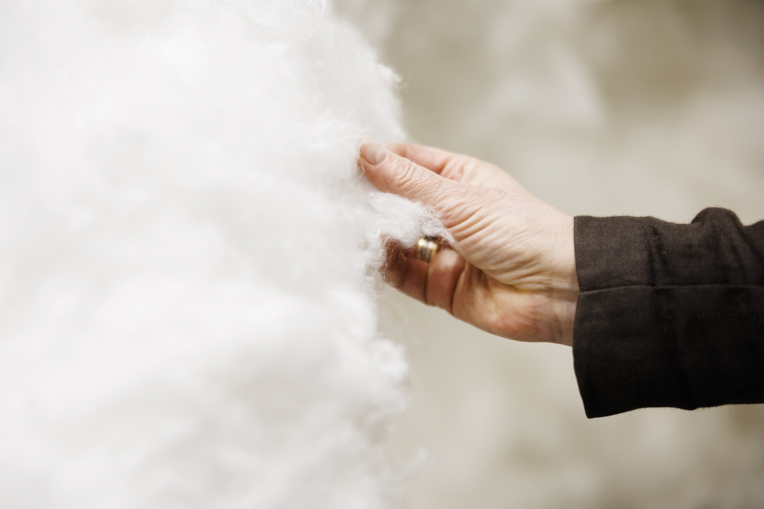Close-up of a hand touching soft, fluffy white material, highlighting texture and detail against a blurred background.
