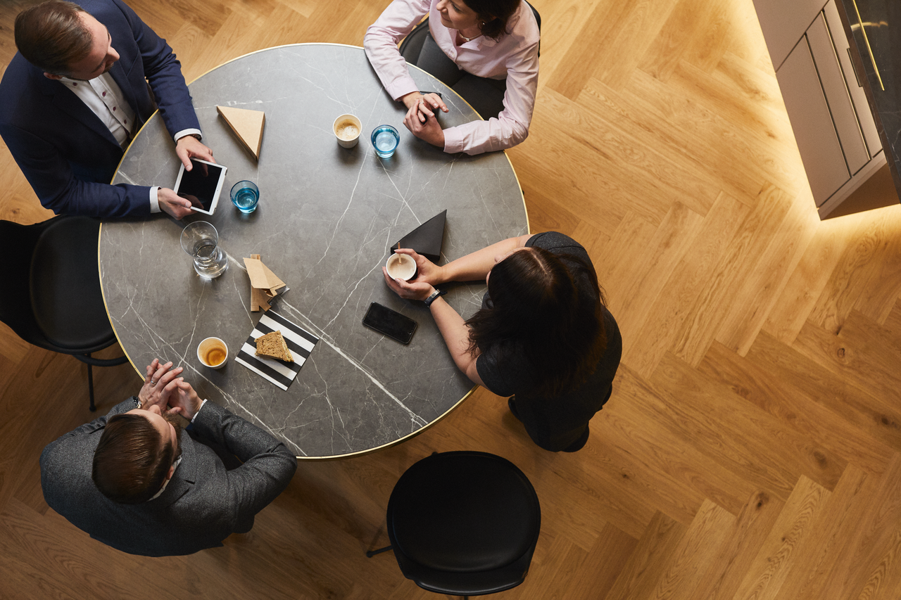 Overhead view of business professionals meeting around a table with coffee and tablets.