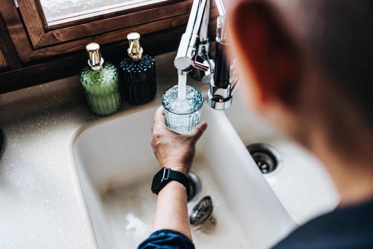 Over the shoulder view of senior Asian man filling a glass of filtered water right from the tap in the kitchen at home.