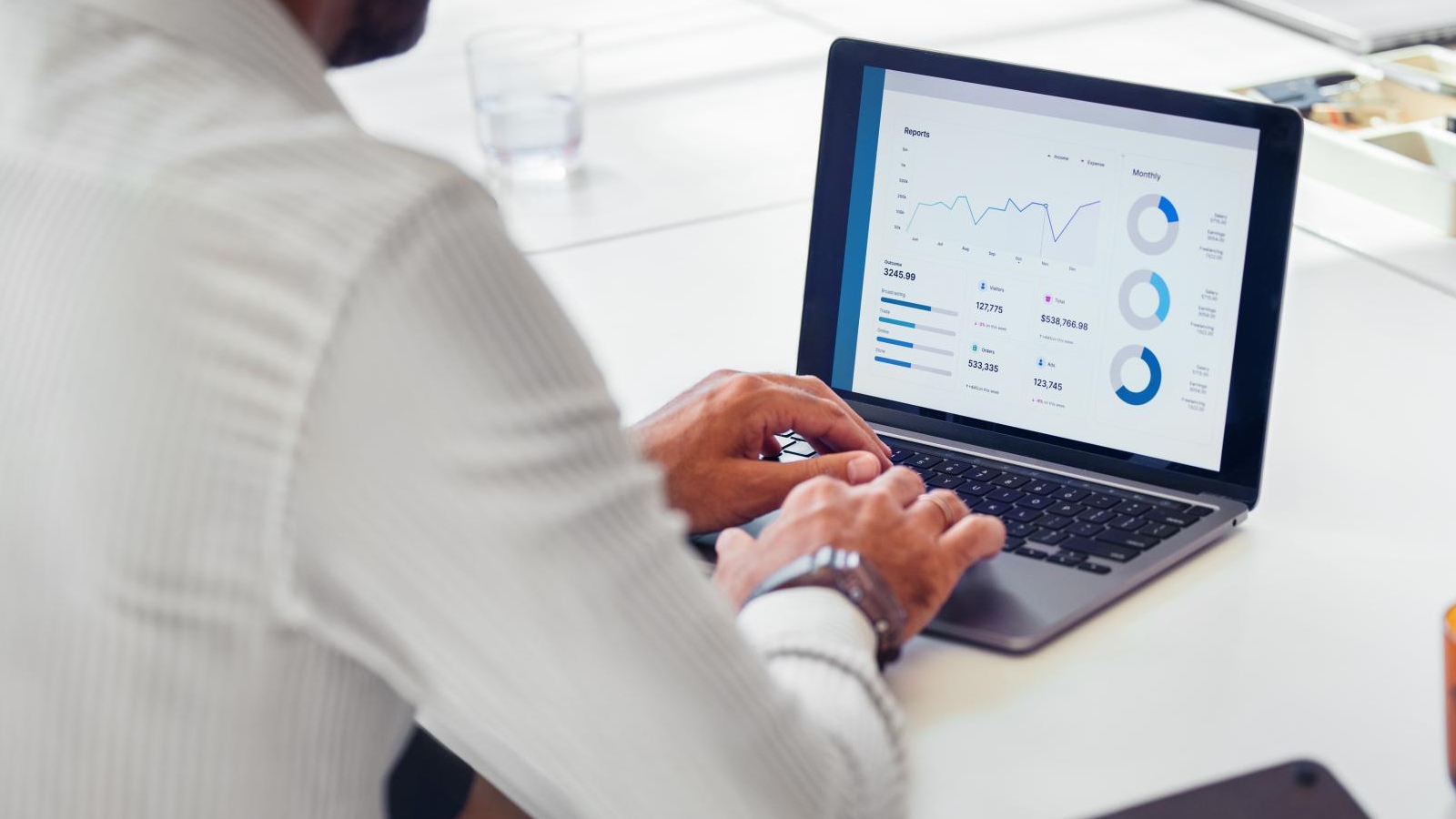 A businessman in a white shirt uses a laptop to analyze financial data and charts, focusing on business growth and strategy development in a modern office setting.