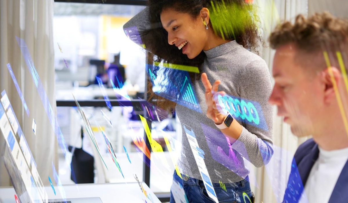 Portraits of young woman and man working in modern office surrounded by multicoloured social media icons and data screens.